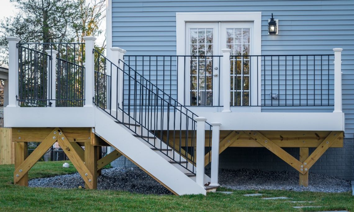 How Material Choices Impact the Longevity of Home Features A raised deck attached to the back of a home. The deck has stairs with white posts and metal railings leading to the ground.