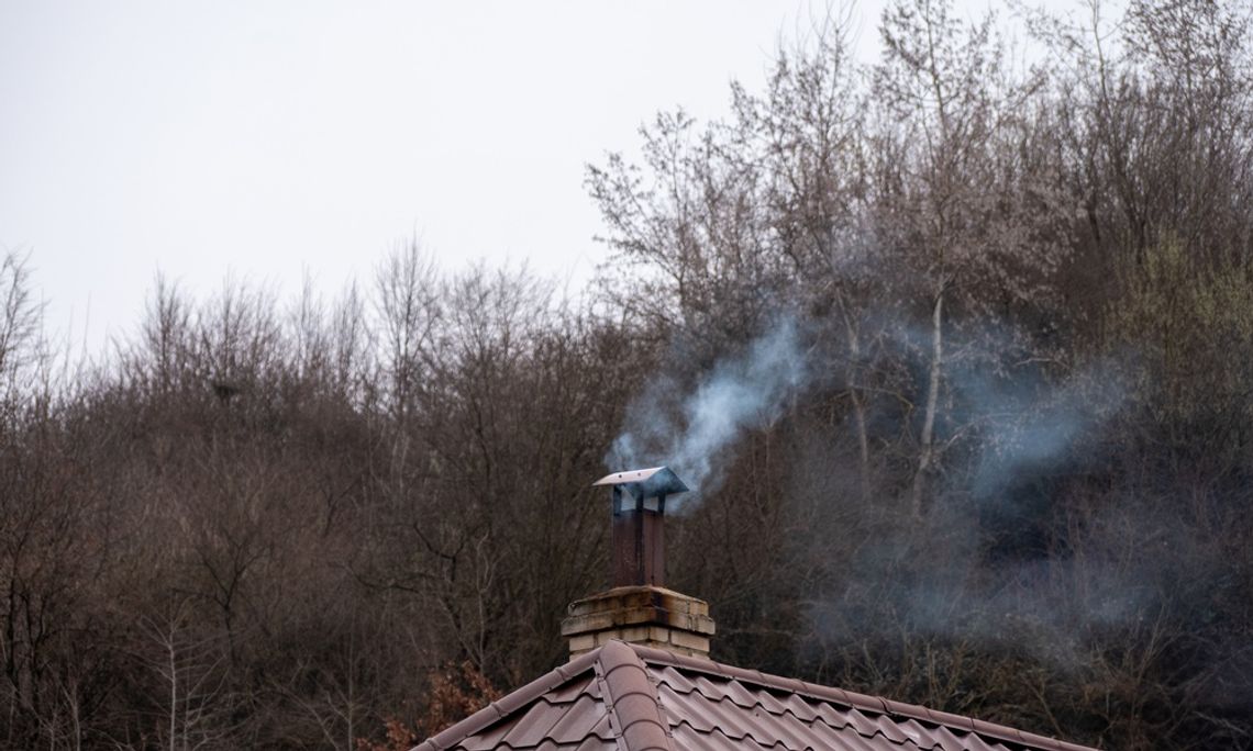 A cloud of smoke billows out from a brick chimney on a metal tiled roof on top of a residential building.
