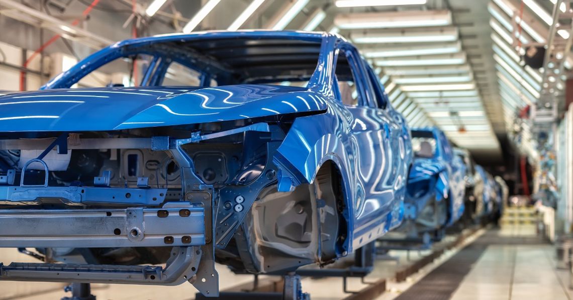 Blue unfinished car bodies move along a brightly lit automotive factory assembly line during vehicle production.