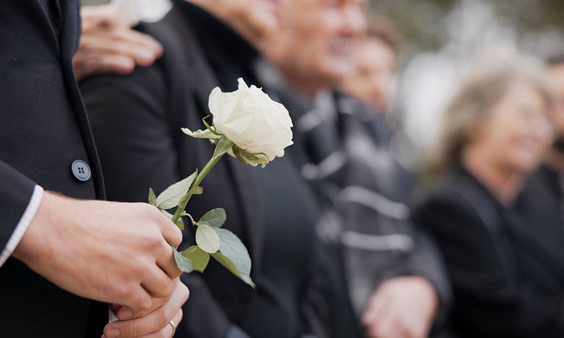 How to Add Elegance and Warmth to Memorial Spaces A group of people wearing black mourning outfits holds a white rose while attending a memorial service.