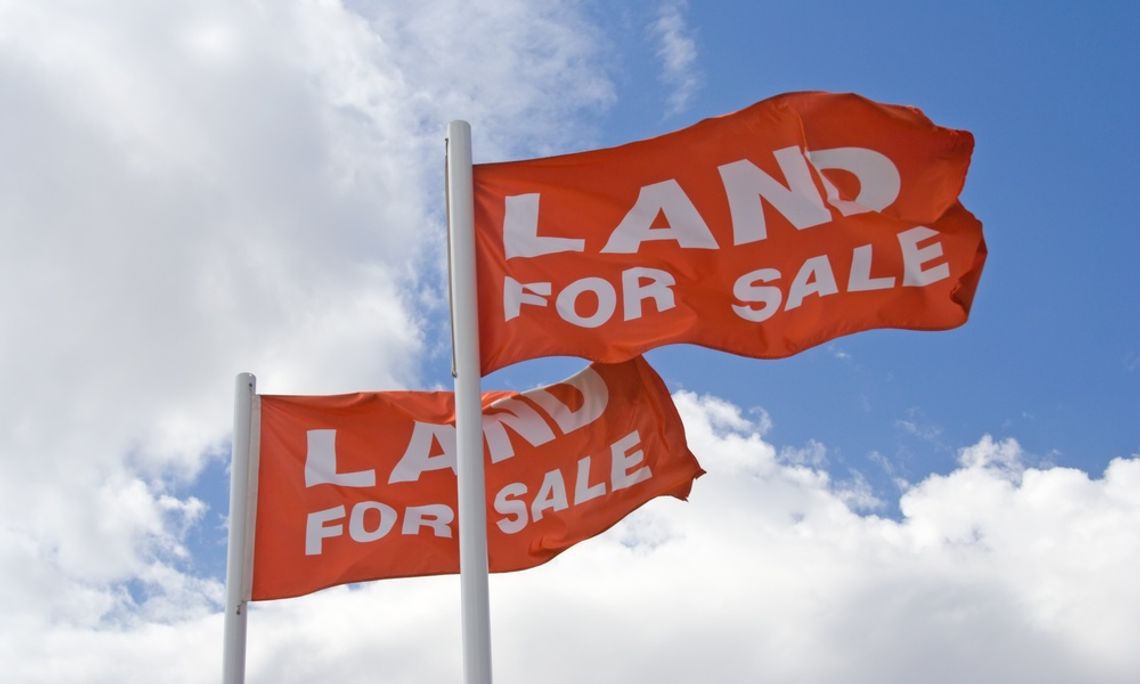 How To Avoid Overpaying When Property Demand Runs Hot Two red flags on white poles waving against a blue sky with large white clouds behind them. They both say "land for sale."
