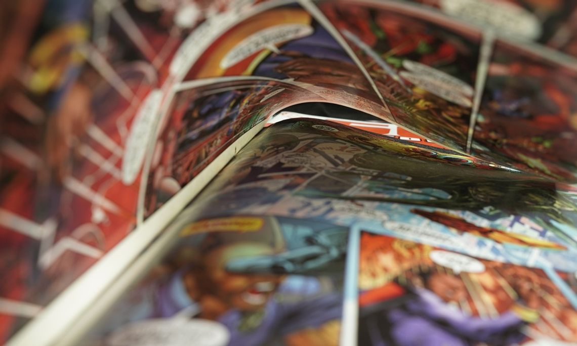 How To Build a Lore Bible for Your Fandom Collection An open comic book curls across a table, showing colorful superhero panels in a soft, close-up blur.
