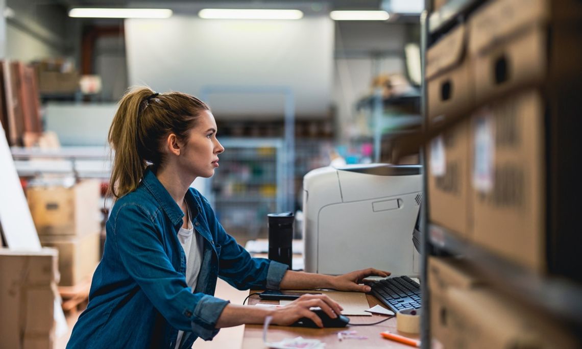How To Build a More Resilient Supply Chain A woman working on her computer as a desk. She is surrounded by tons of boxes on shelves and on the floor.