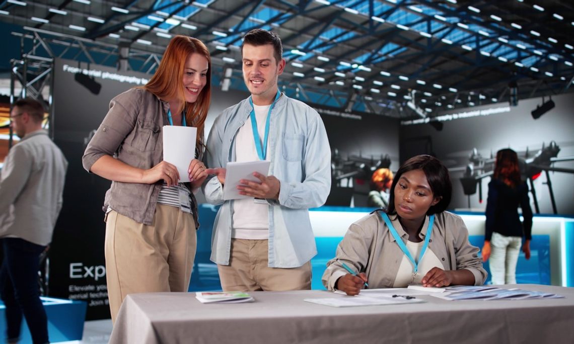 How to Build Buzz for Your Next Trade Show A group of three people wearing light blue lanyards and holding flyers prepare to present in a trade show conference.