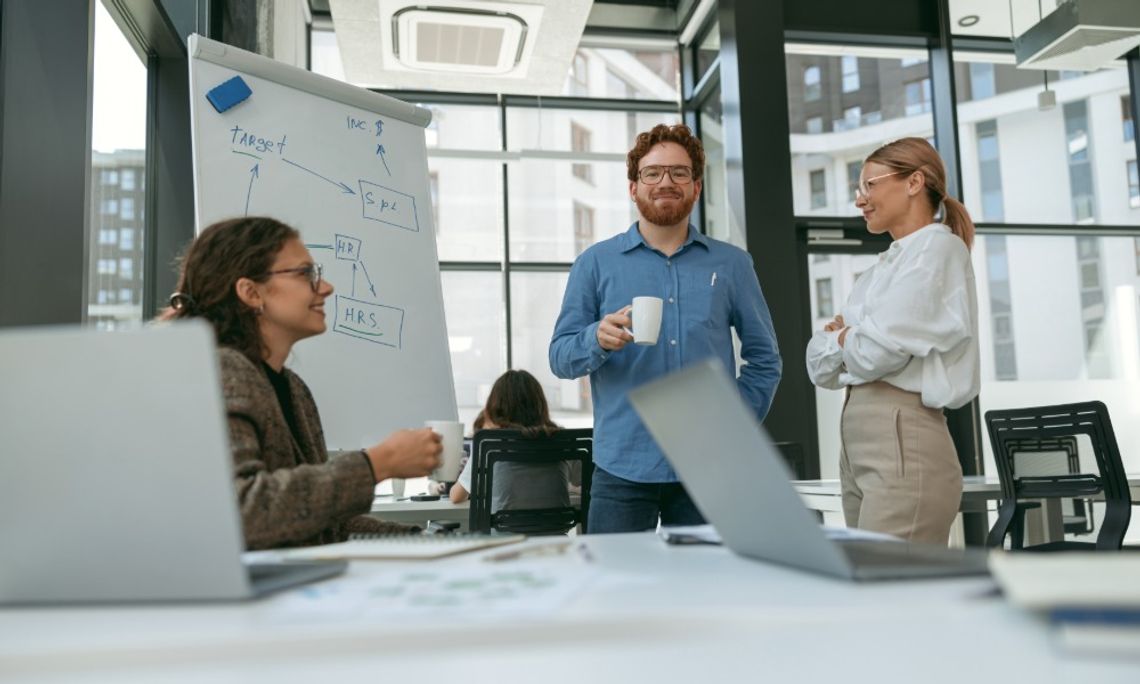 How To Create Better Outdoor Break Areas for Employees Coworkers gather for a casual office discussion beside a flip chart, while laptops sit open in the foreground.