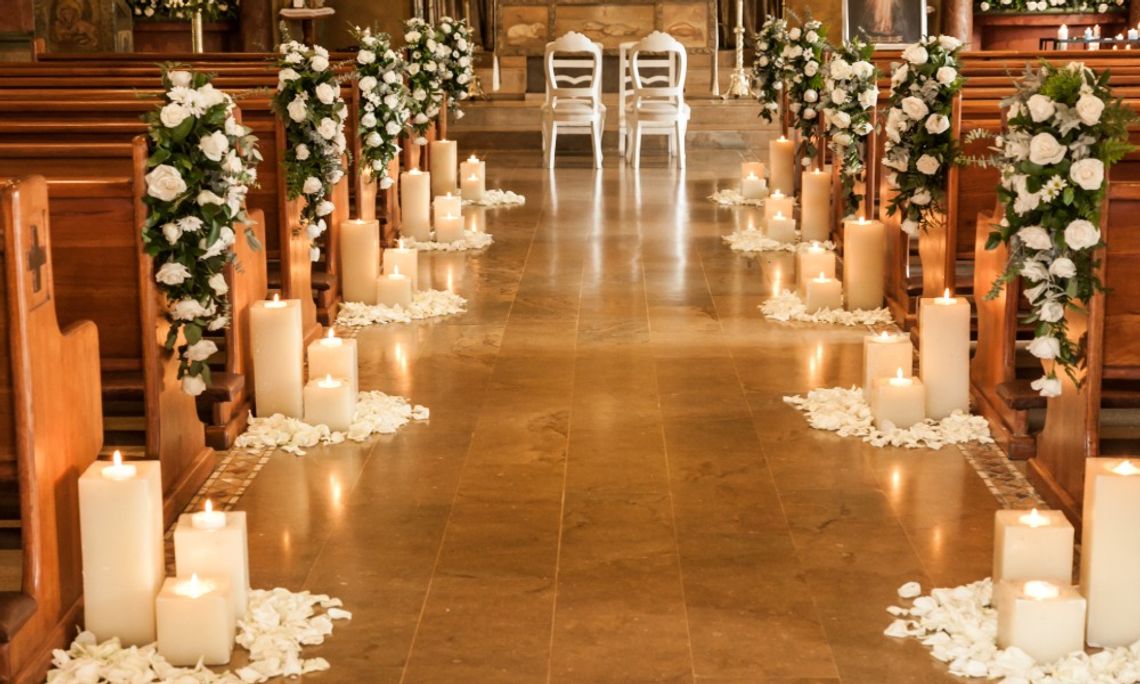 How To Decorate Your Wedding Ceremony Like a Pro A candlelit wedding aisle lined with white floral arrangements, rose petals, and wooden pews leading to an altar with chairs.