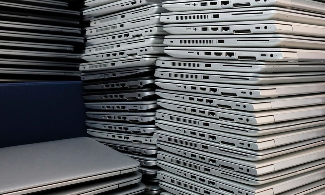 A close-up of dozens of silver laptops. They're arranged in four towering stacks and showing cable ports.