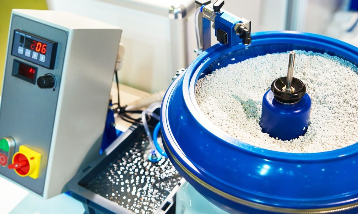 A blue vibratory finishing bowl full of small media in a factory. A small tank of water connects to the finishing bowl.