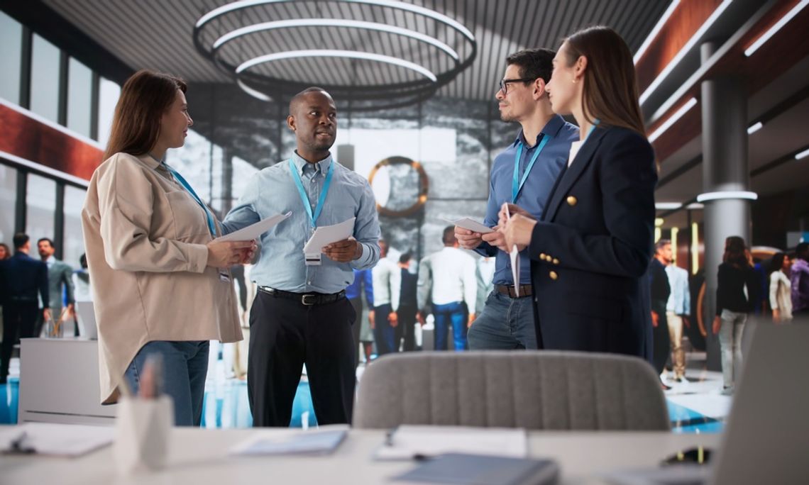 How To Organize Your First Trade Show Booth Four professionals wearing teal lanyards holding documents in the middle of a busy trade show floor.