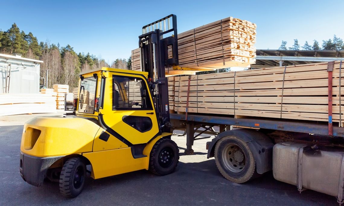 How to Prevent Damage to Materials on Construction Sites The sun shines down on a yellow forklift as it loads lumber construction materials onto a truck's bed.