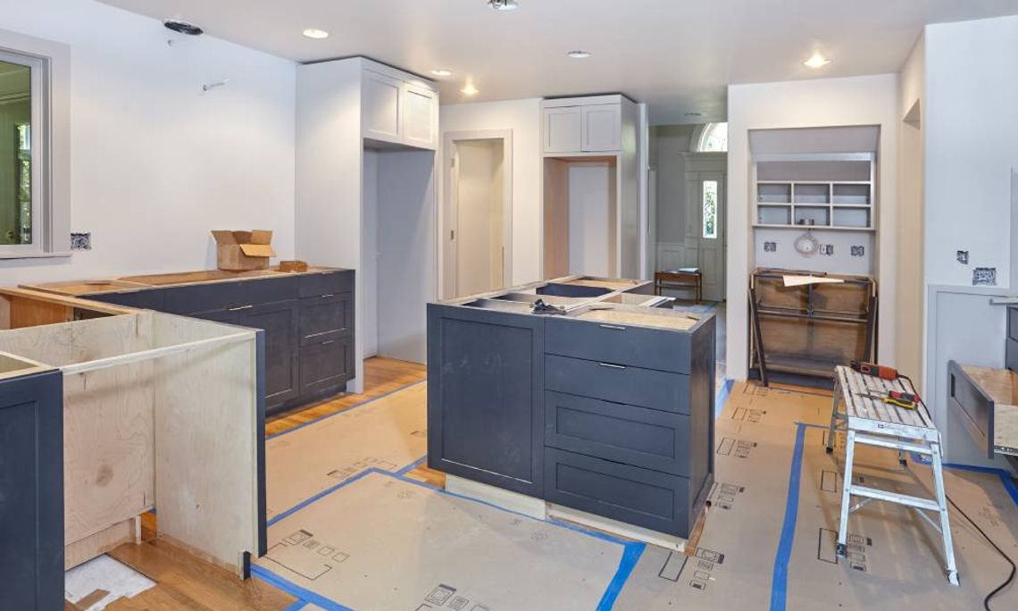 Custom cabinets being installed in a kitchen, some finished and some unfinished. Cardboard is laid out on the floor.