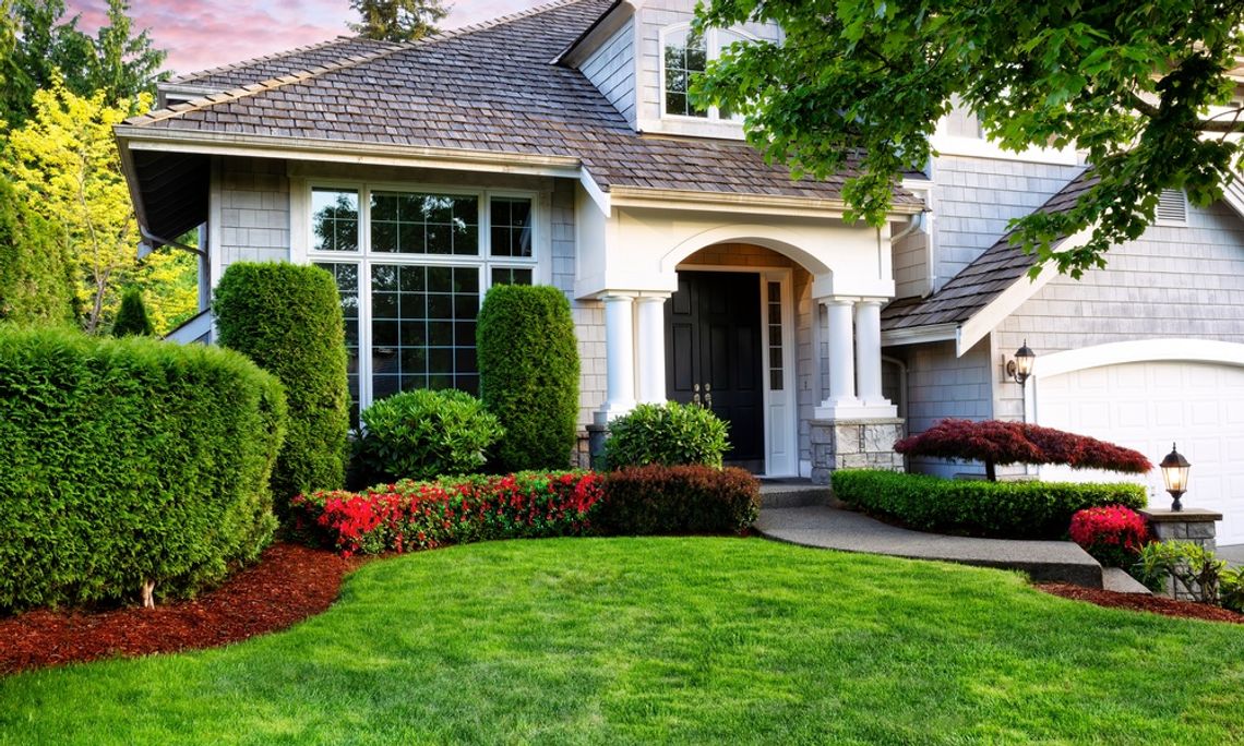 How To Refresh Your Landscaping Without a Major Renovation A landscaped front yard with manicured shrubs, red flowering plants, and a green lawn leading to a home entrance.