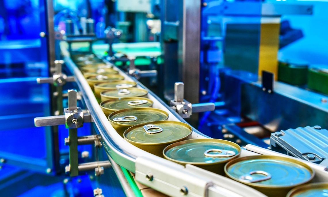 A close-up of a narrow conveyor belt in a distribution facility transporting round cans of food with pull tabs.