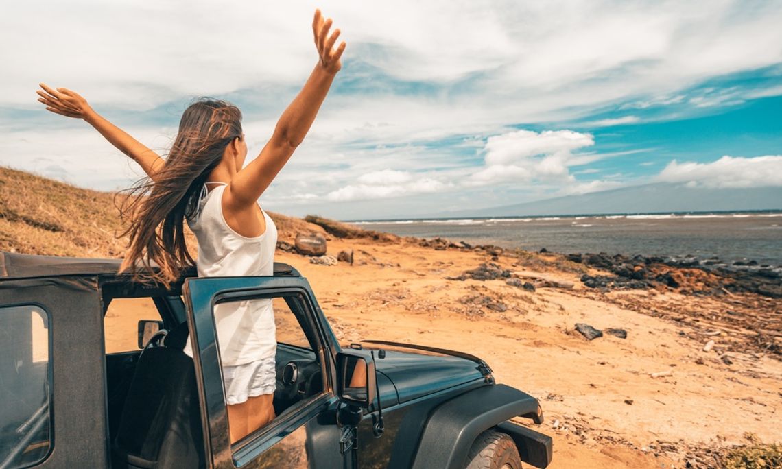 How You Can Elevate Your Next Off-Roading Trip A woman standing up in the passenger seat of a truck with her arms in the air. She is parked in some dusty plains.