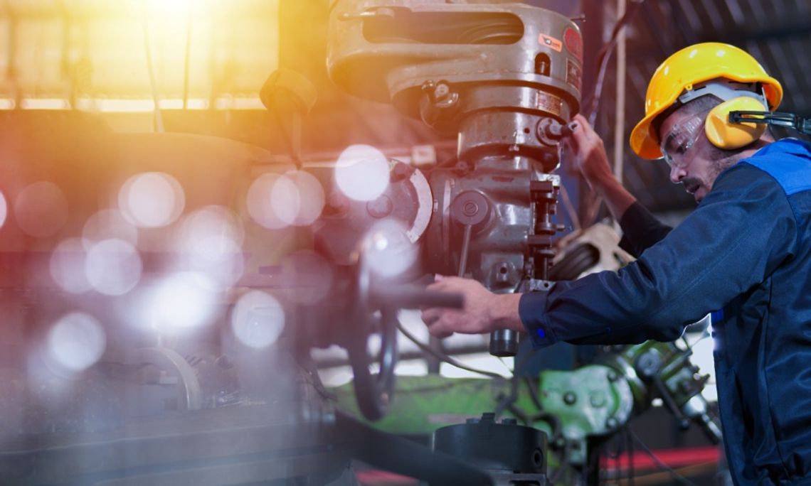 Important Safety Tips for New Operators of Heavy Machinery A factory worker wearing a hard hat and ear protection while he is working with a large piece of machinery.