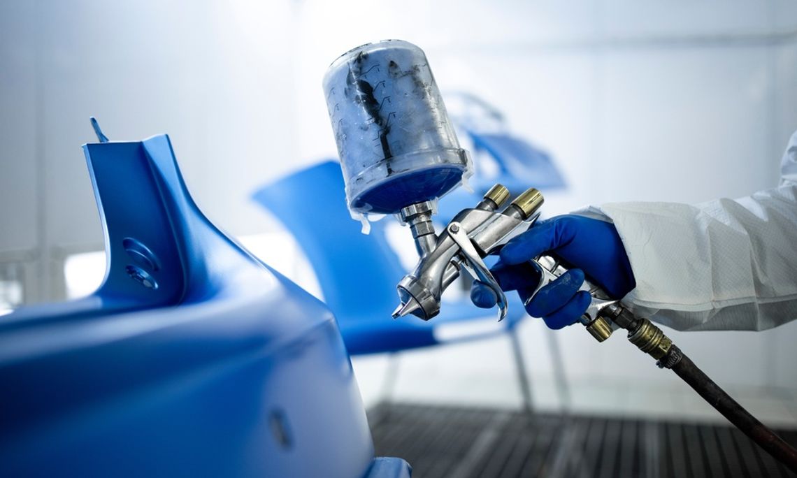 Industries That Rely on Pneumatic Automation A worker in protective gear uses a spray gun to apply blue paint onto a molded component in an industrial paint booth.