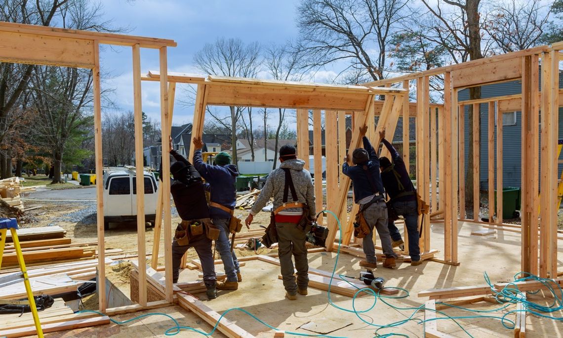 A group of construction workers working together to erect the frame of a new house that they are putting together.