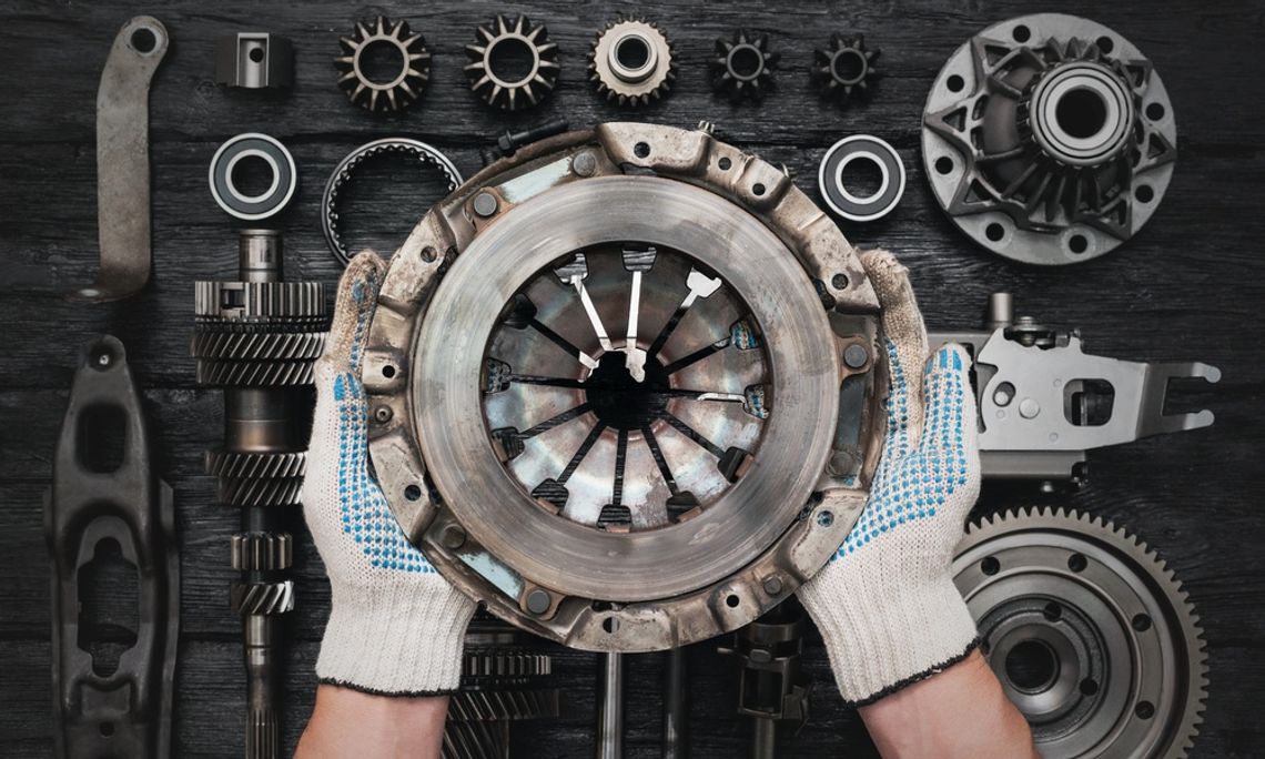 An overhead view of a person with white gloves holding a clutch basket over a black table with other clutch parts.