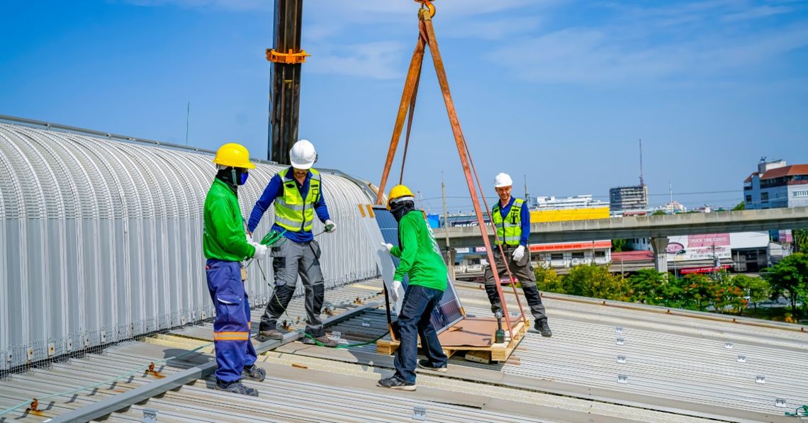 Must-Know Lifting Techniques for Construction Crews Four construction workers wearing blue-and-green uniforms on a roof using a crane to lift building materials.