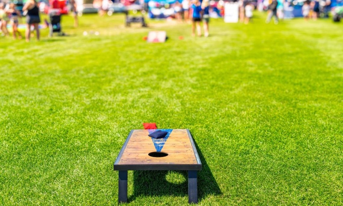 At a large outdoor gathering, there is a cornhole board in a field with two bags sitting on top of it.