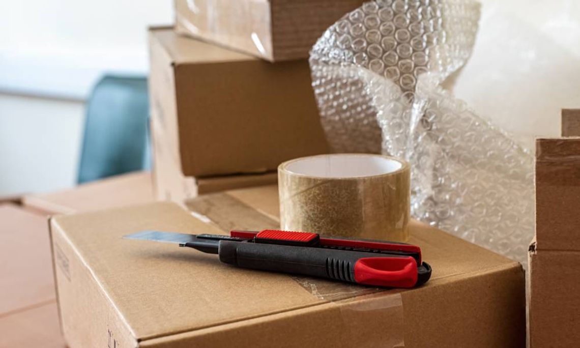 A selection of packaging and shipping supplies, such as a cardboard box, packing tape, bubble wrap, and a box cutter.