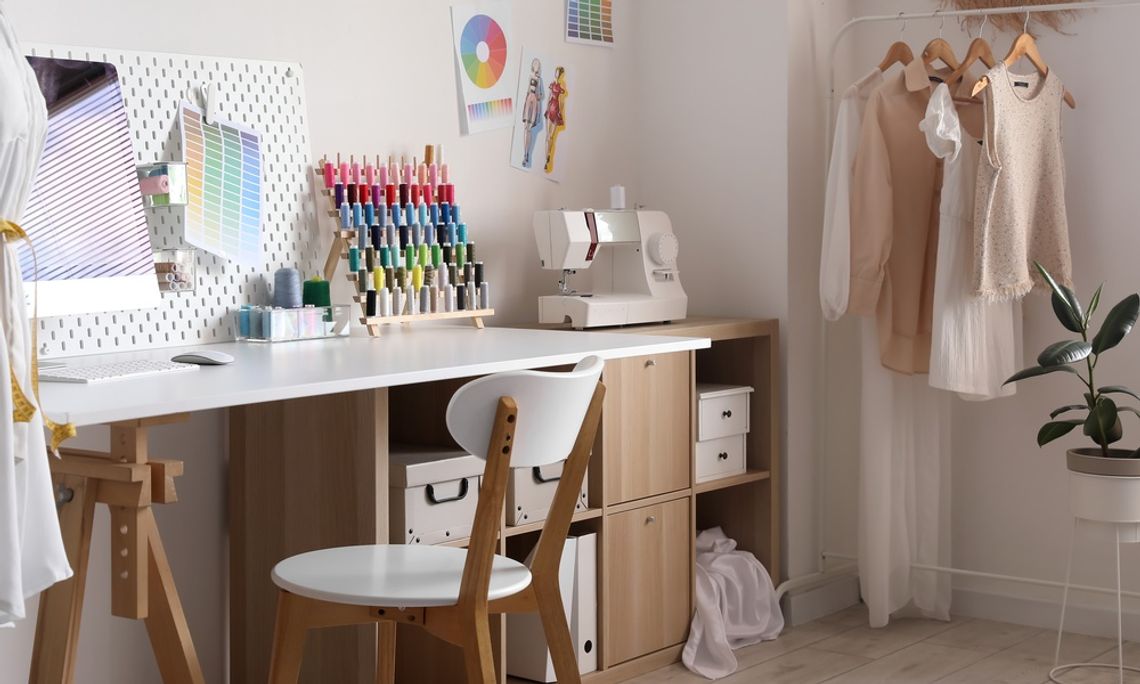 A white table next to a wall with a matching chair, holding multiple colored threads, a sewing machine, and some boxes.