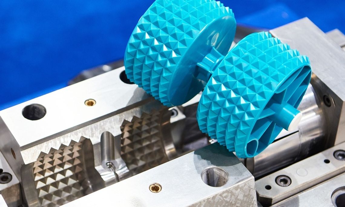 A finished, cyan plastic part with two spike-covered cylinders sitting on top of its silver metal mold.