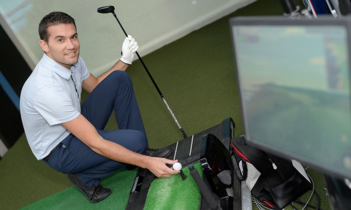 Sports Training Technologies Every Athlete Should Know About A man smiles as he positions a small golf ball on his simulator. He holds a golf club in his other hand.