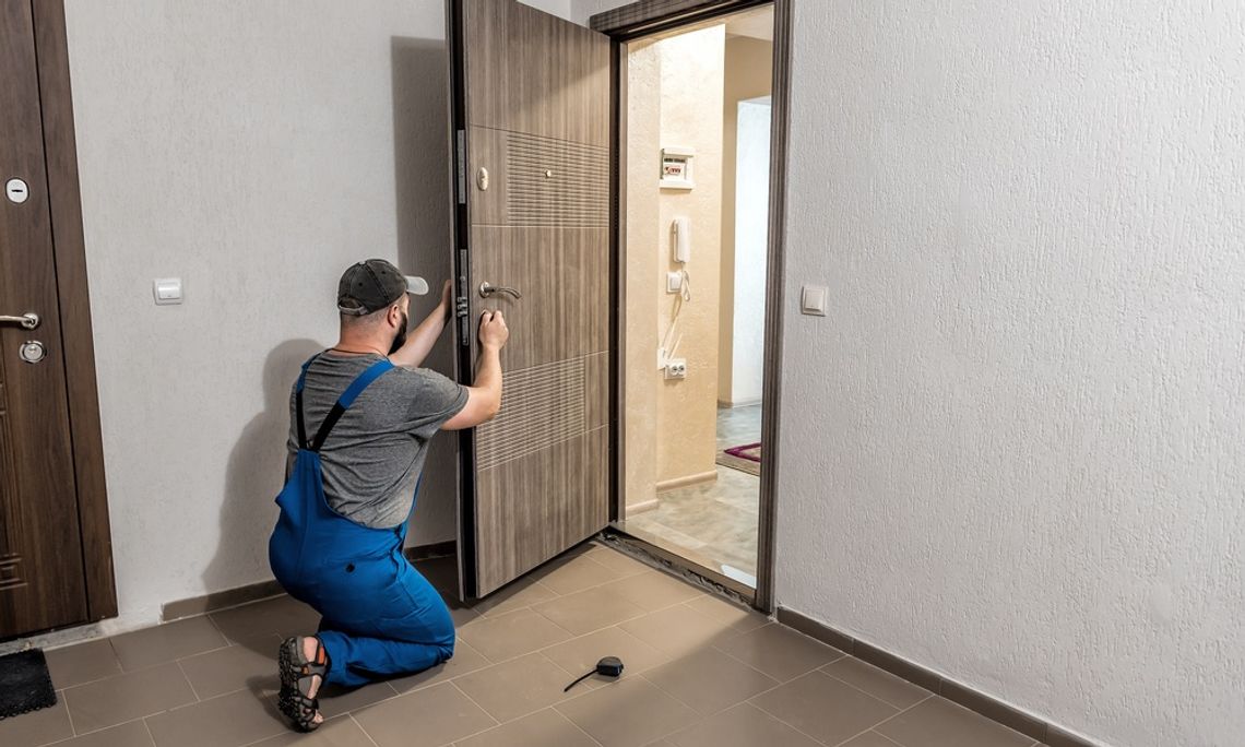 Surprising Ways You Can Make Your Home More Energy Efficient A person wearing a hat kneeling and installing a large beige front door in the entryway of a modern home.