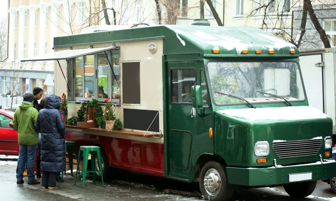 The Best Tips for Winterizing Your Food Truck A green food truck parked outside during the daytime during winter. Three customers wait outside the truck.