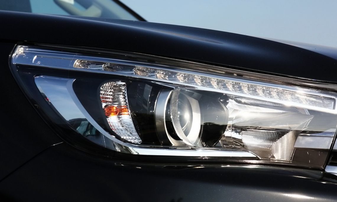 The Different Types of Lights You Can Install on a Truck A close-up of a black pickup truck headlight with a circular projector lens, chrome reflectors, and a narrow LED strip.