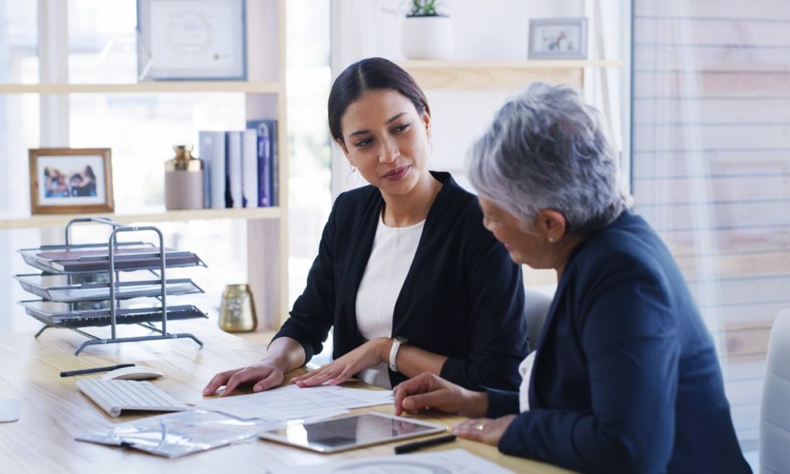 The Steps That Go Into Making an Estate Plan An older woman is sitting next to a younger woman at a desk that has several pieces of paper on it.