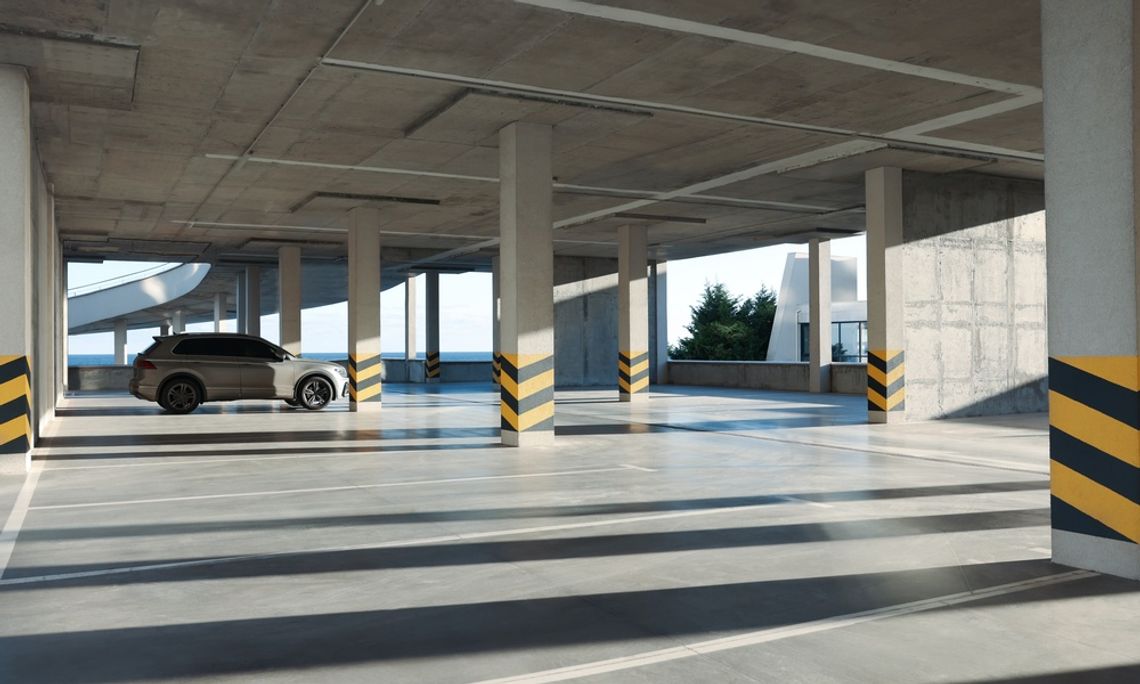 Things To Know Before Building a Parking Garage A gray car parked alone between two pillars in a parking garage. Bright sunlight shines into the parking structure.