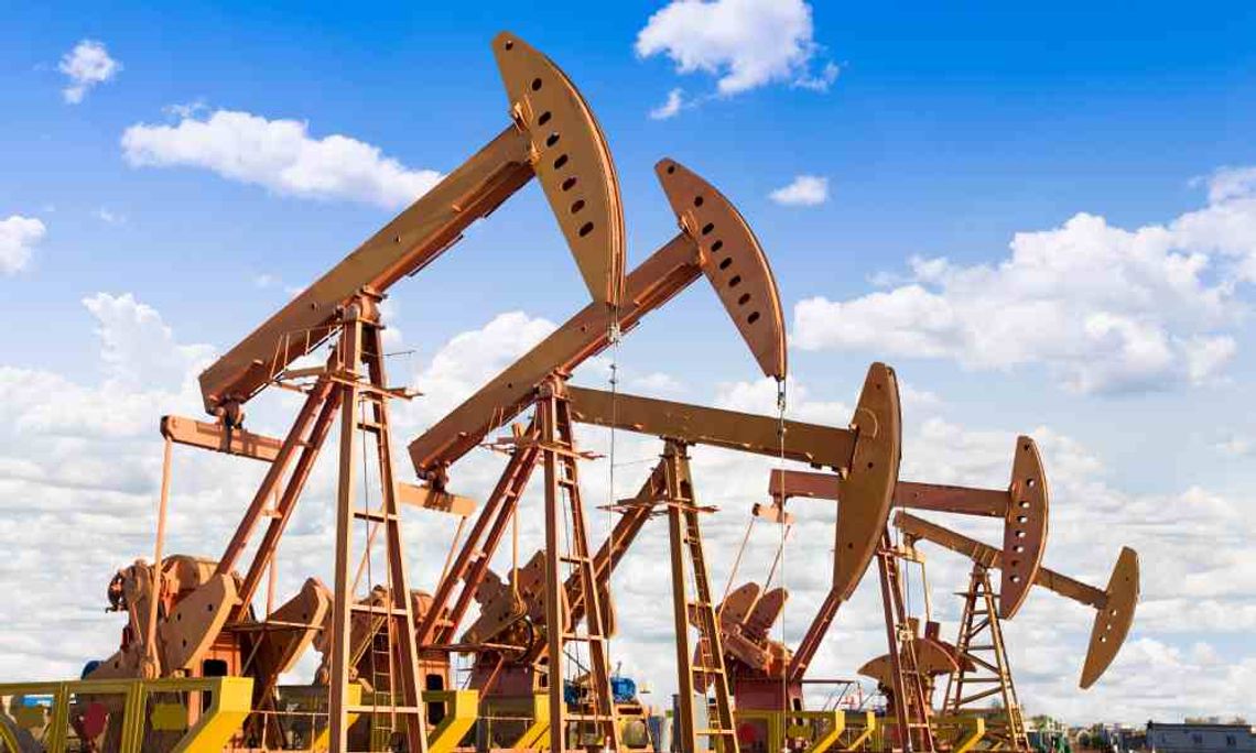 A panoramic view of oilfield equipment. There are five large oil derricks with storage tanks and pipelines near them.