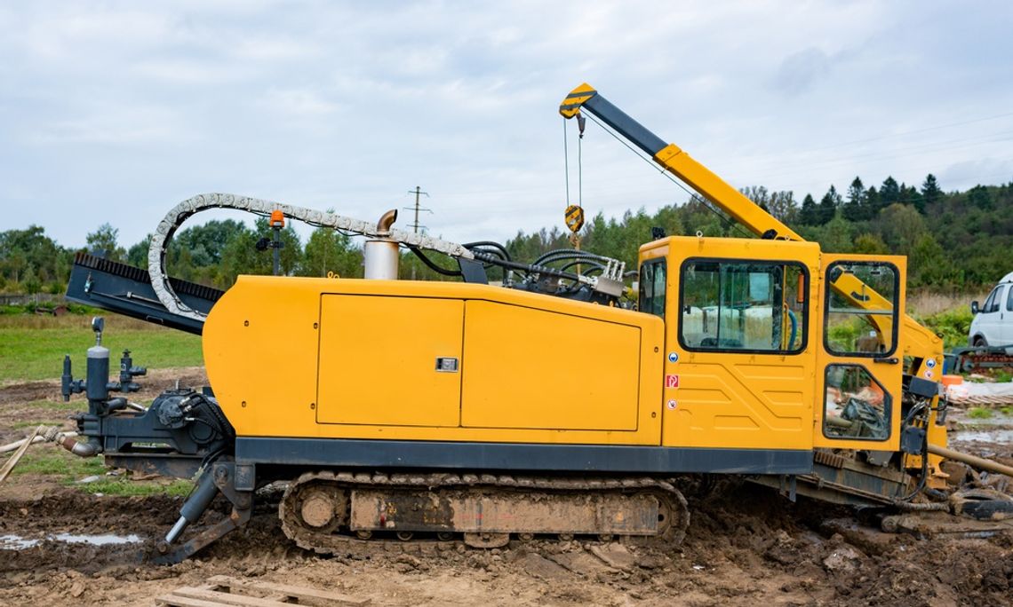 A yellow horizontal directional drilling machine drills on the ground underneath a bright blue sky.