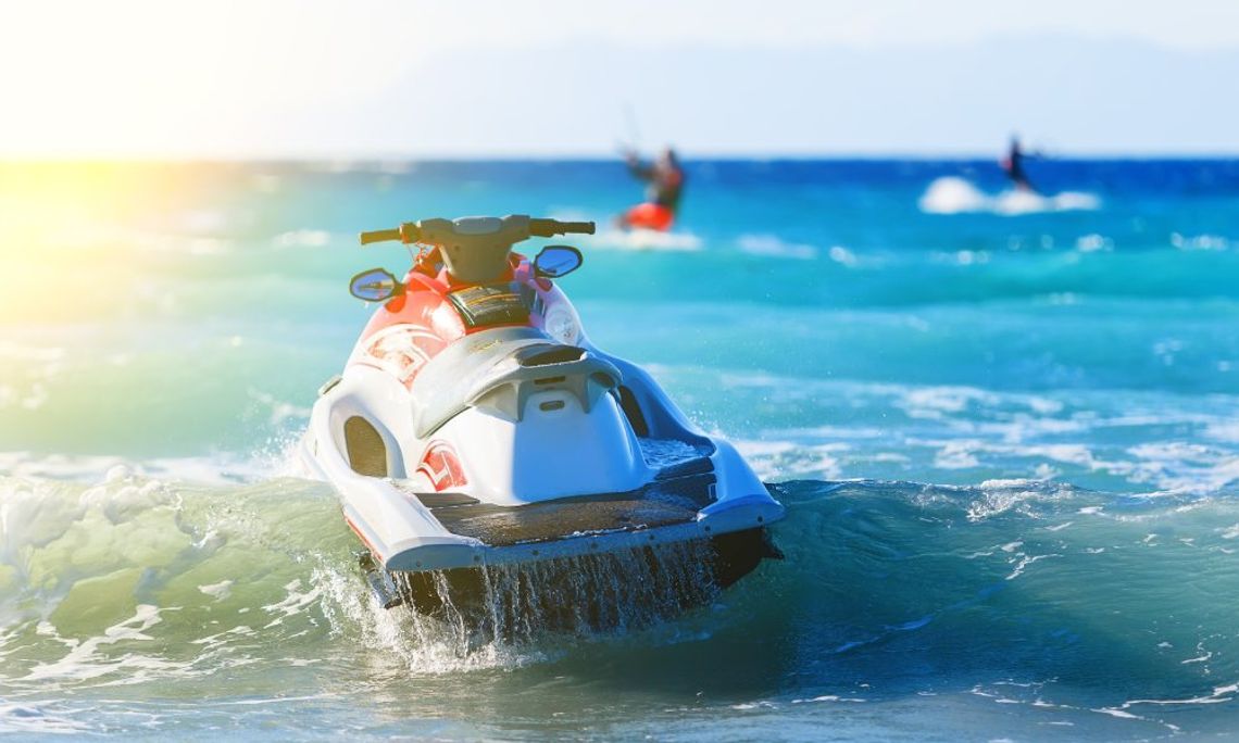 A jet ski floats on top of some water with other people having fun in the background. The sun shines from the left.