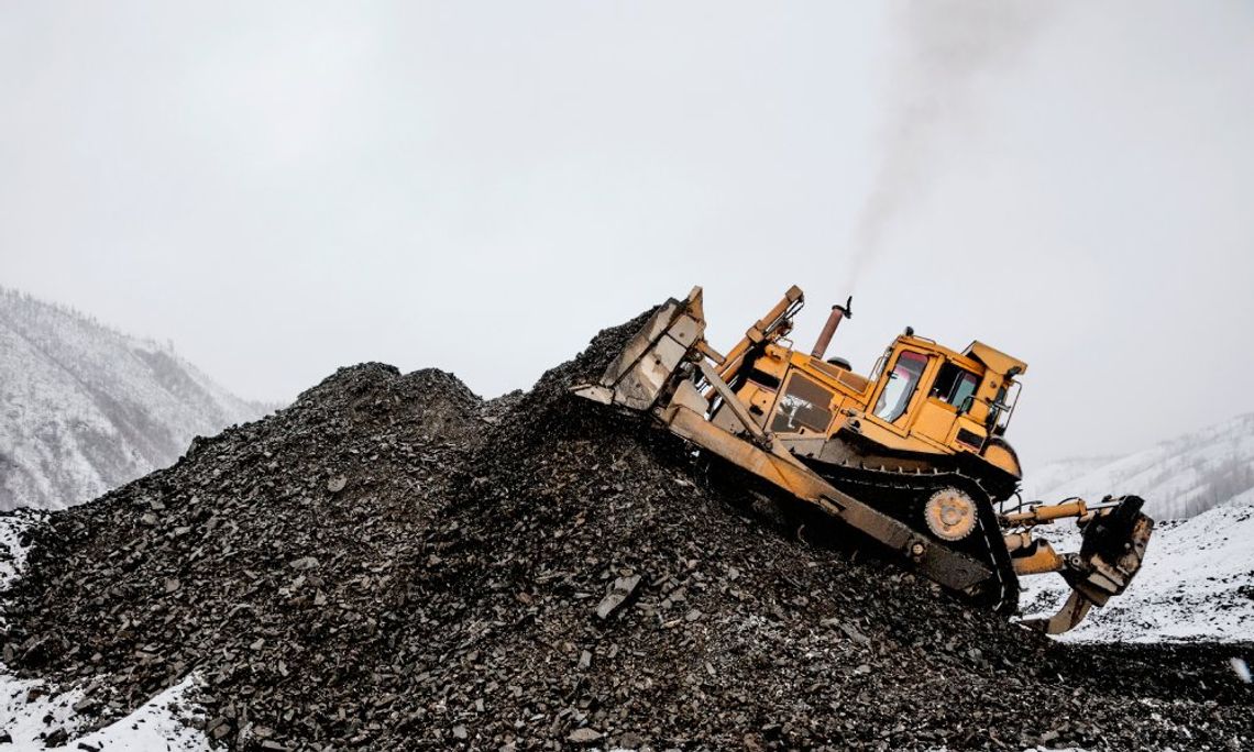 A large yellow bulldozer moves mining debris into a hill in an industrial mining area covered in snow.