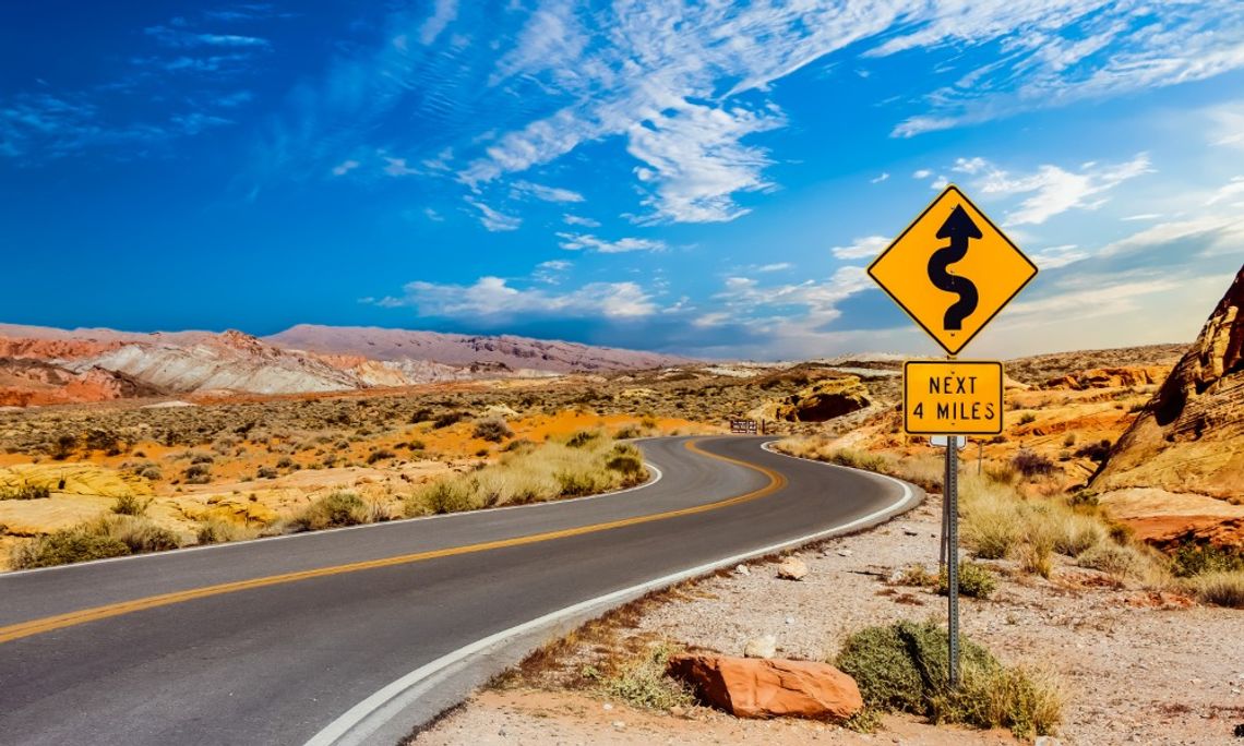 Winding road through a rocky desert landscape with a yellow curves warning sign indicating winding road for four miles.