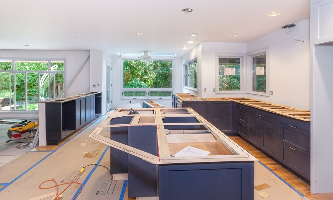A kitchen that’s under renovation; all the counters are missing from the cabinets, and cardboard covers the floor.