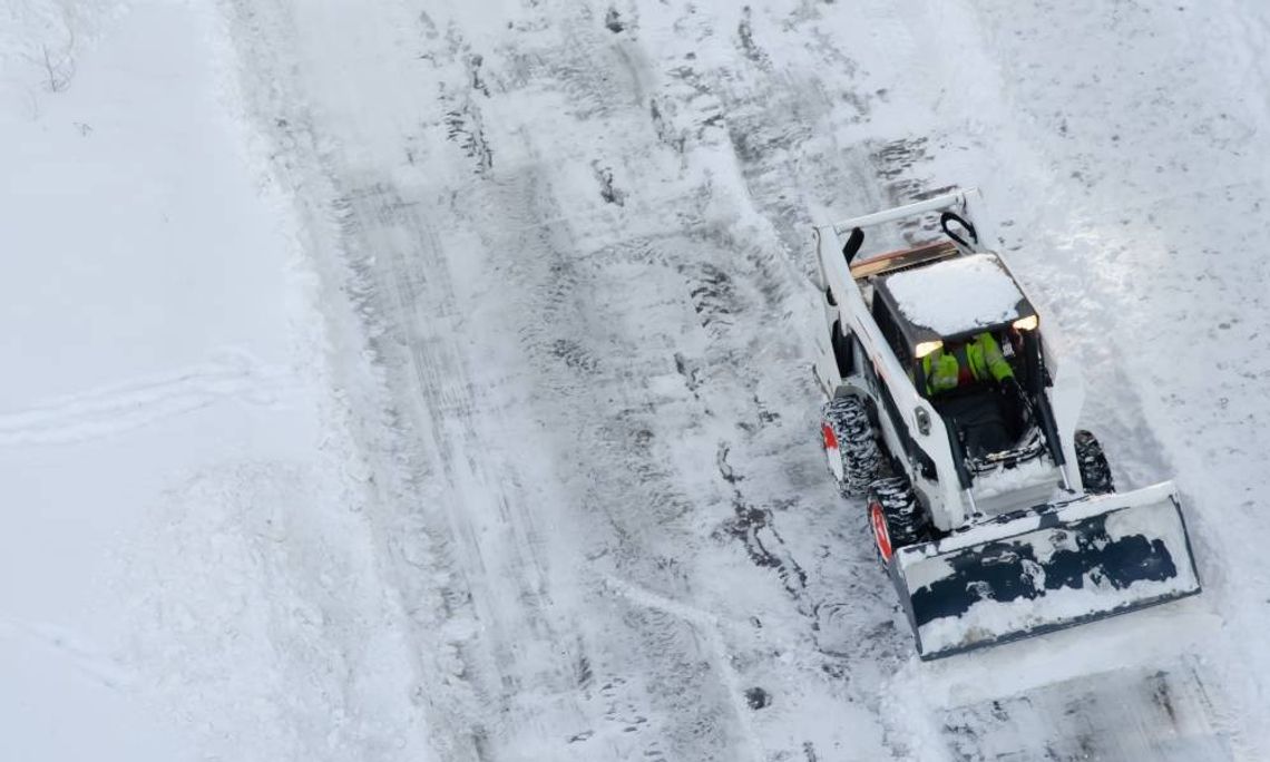 An overhead view of a compact tractor with a front-mounted snow plow operating in frigid, snowy winter conditions.