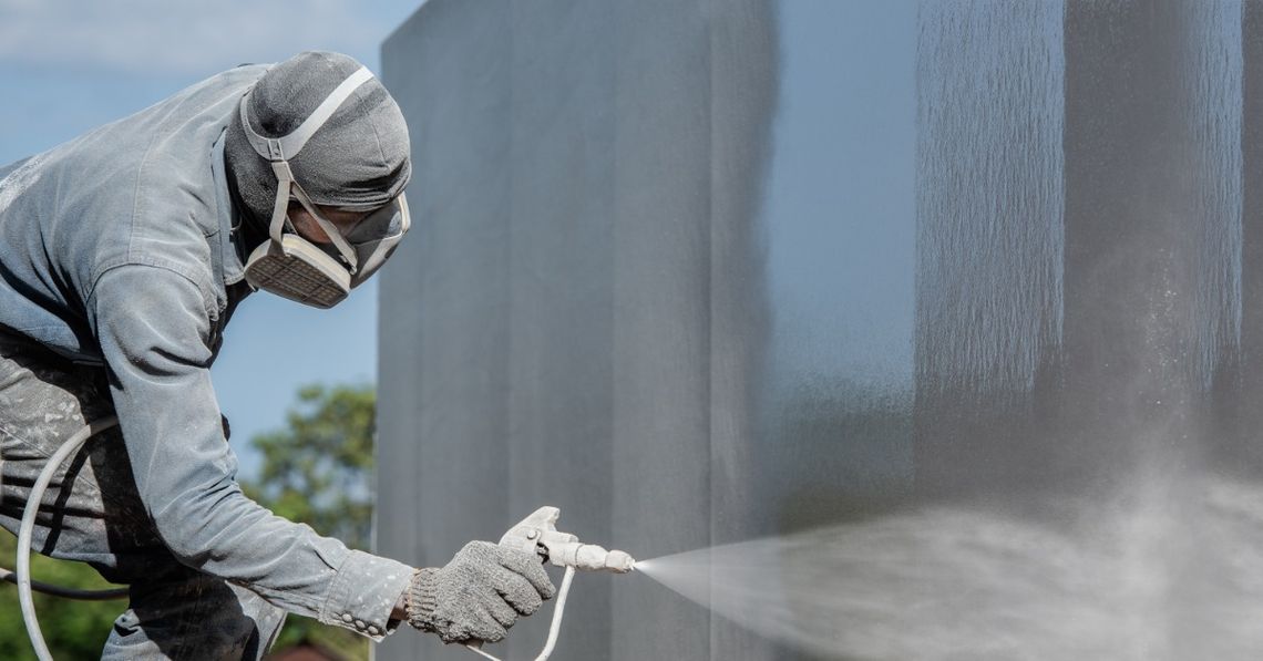Understanding When To Use Tungsten Carbide Coatings Worker wearing protective gear spray-coats a large metal surface with an industrial coating outdoors.