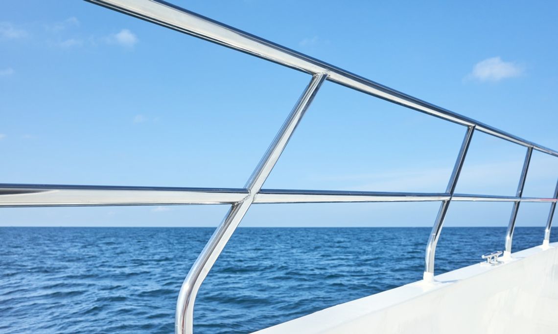 A close-up view shows a shiny stainless steel boat railing on a white boat that is out on a large body of water.