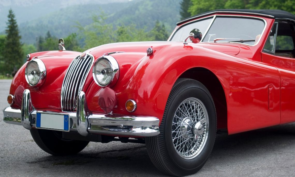 Ways To Improve a Classic Car Without Losing Its Character A red classic convertible car with chrome details and wire-spoke wheels parked near a wooded mountain area.