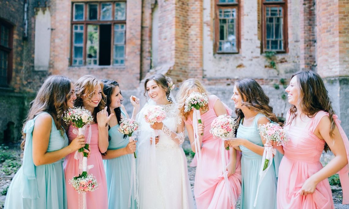 Ways To Make Your Bridesmaids Feel Appreciated A bride stands outside beside her six bridesmaids; three bridesmaids wear blue dress and three wear pink.