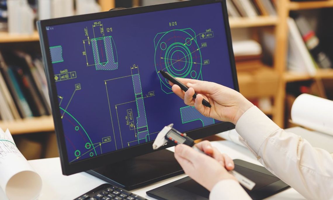 A pair of hands holds a stylus and a measuring tool while pointing to a CAD design displayed on a computer screen.