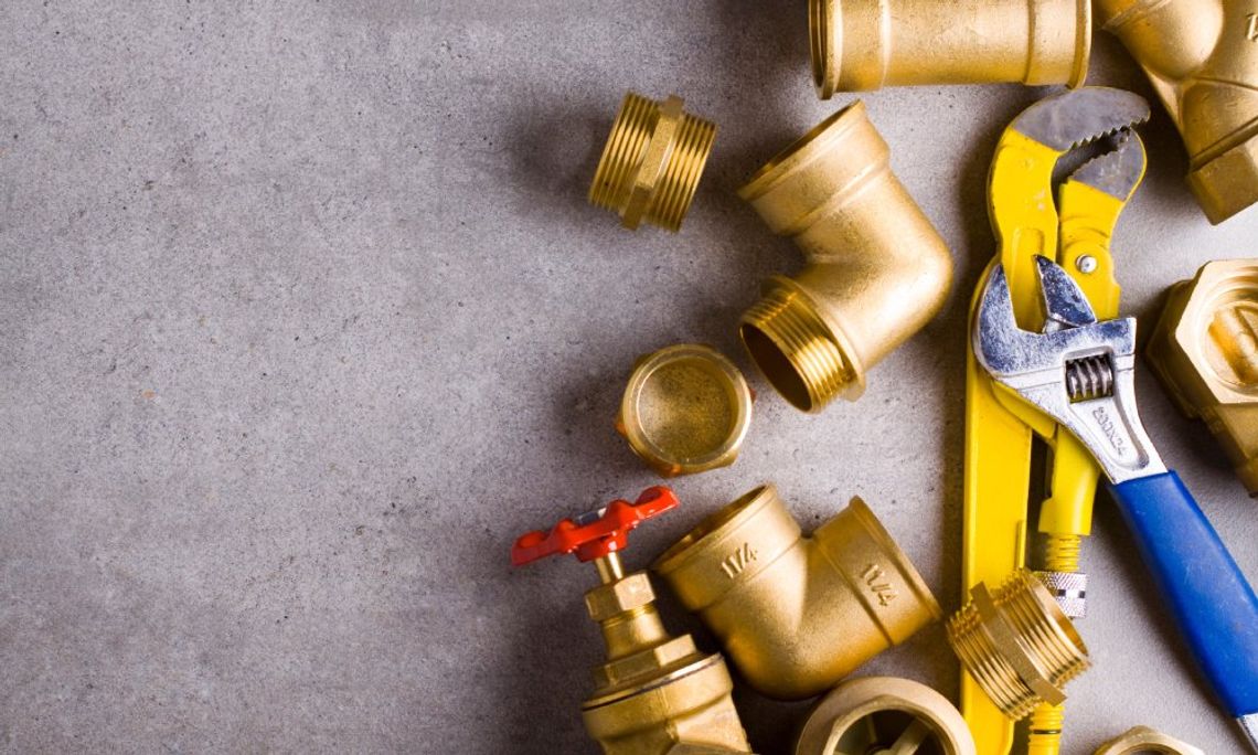 A yellow and a blue wrench, a pair of working gloves, and brass fittings placed on a rough, textured floor.