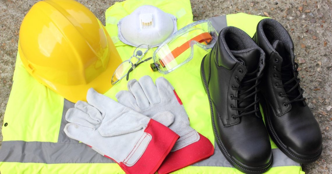 What New Construction Workers Need To Know About PPE A collection of personal protection equipment including a hard hat, work vest, gloves, and a pair of boots.