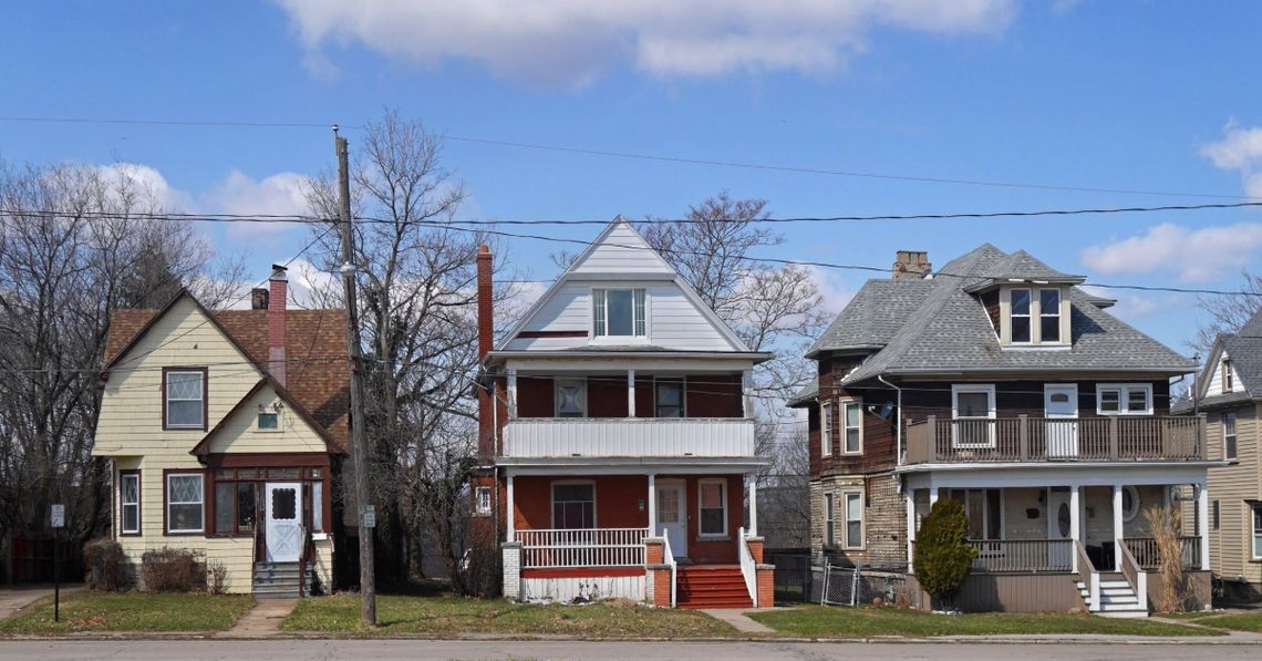 A row of three slightly older looking houses on a street block. There are trees in between each house.