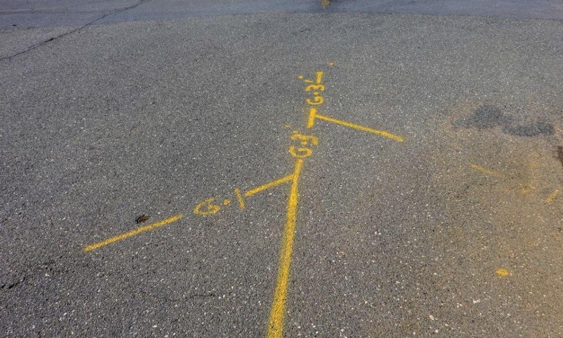 A patch of concrete with yellow spray paint indicating utility lines nearby. The lines also have numbers and letters.