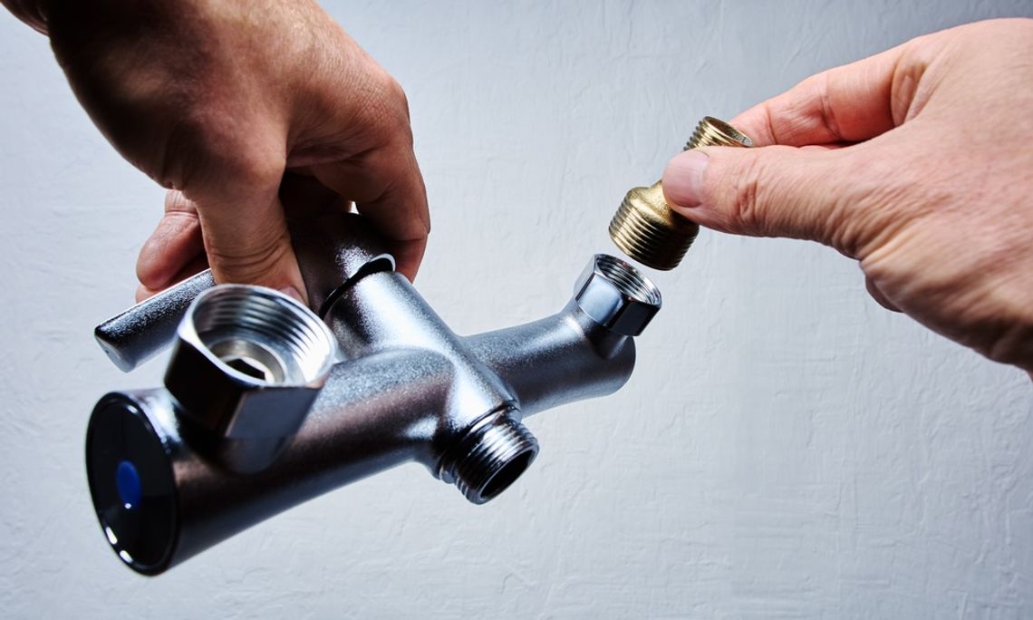 A person attaching a threaded brass component to a silver plumbing fixture in front of a white background.
